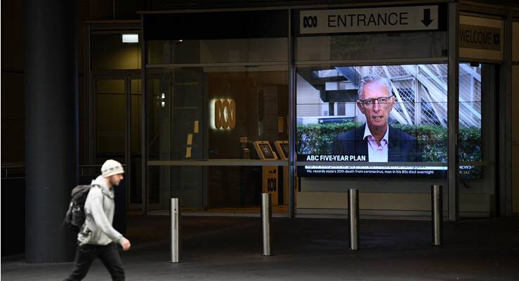 man walks past ABC entrance with television screen showing press conference about job cuts
