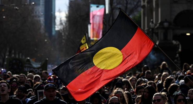 A First Nations flag over a crowd (Image: AAP/James Ross)